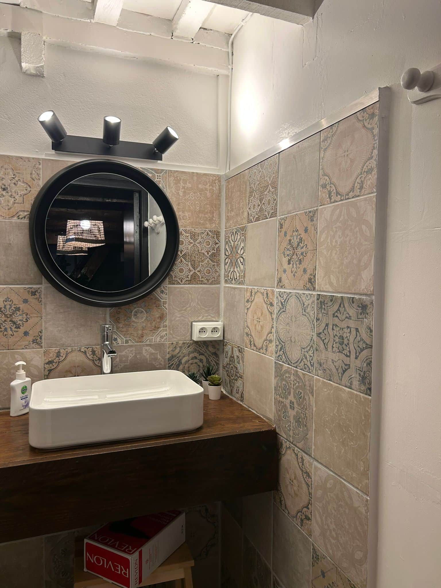 Une salle de bain avec un lavabo blanc, un miroir rond et des carreaux à motifs.