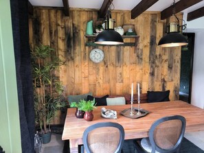 Un coin repas en bois avec une table, des chaises et un banc. On peut voir des plantes en pot, une assiette décorative et un chandelier sur la table.