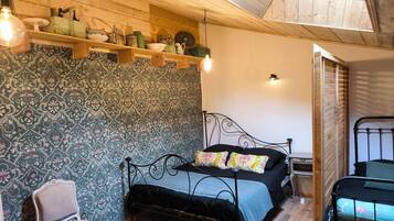 Une pièce comprenant un lit, une chaise, une étagère avec divers objets et un mur orné d’un motif.