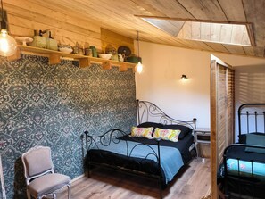 Une pièce comprenant un lit, une chaise, une étagère avec divers objets et un mur orné d’un motif.