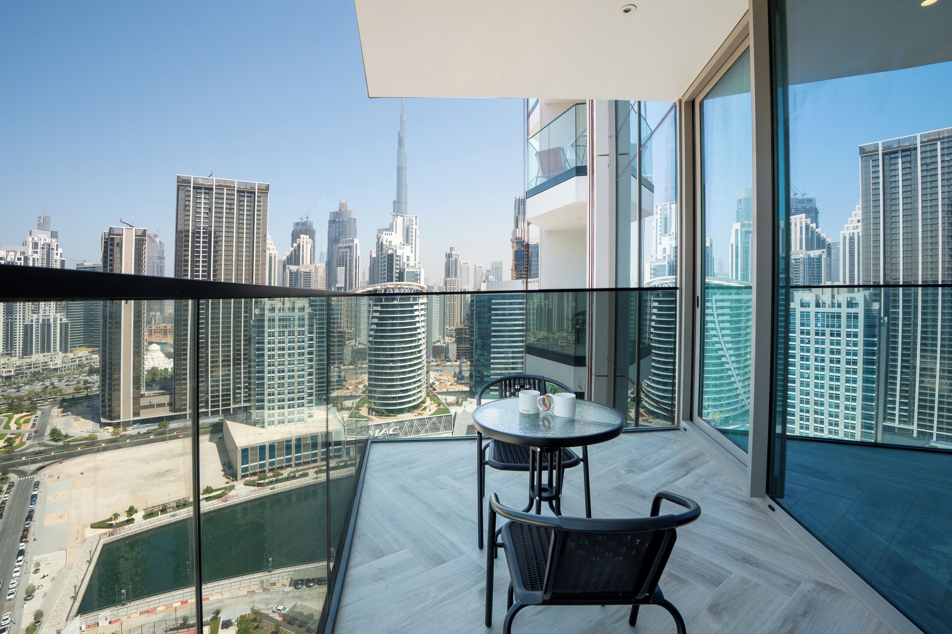 Un balcone con ringhiera in vetro che si affaccia su un panorama urbano con edifici moderni e un fiume.
