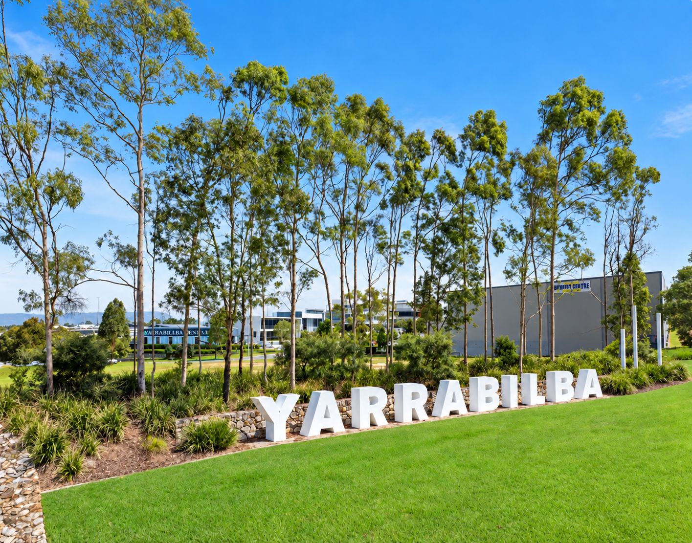 Un letrero con la palabra 'YARRABILBA' en letras grandes, rodeado de césped cuidado y árboles.