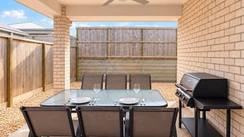 An outdoor patio with a table set for two, a grill, and a ceiling fan.