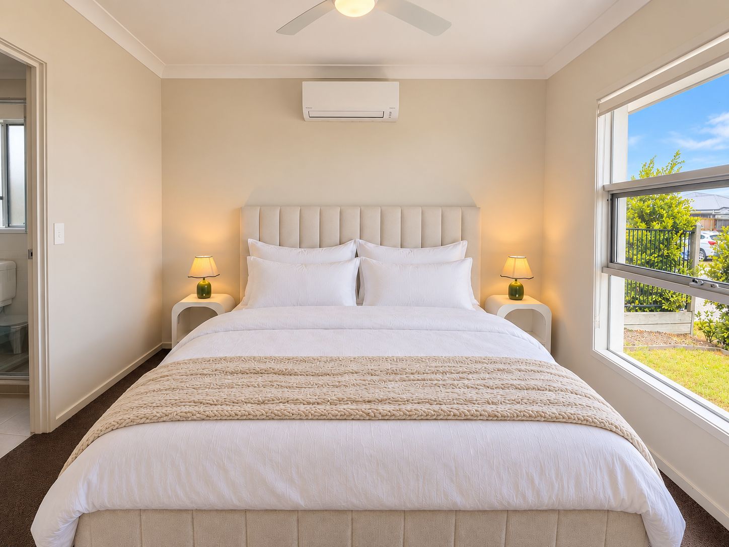 A bedroom with a bed, two bedside lamps, a ceiling fan, and a window with a view.