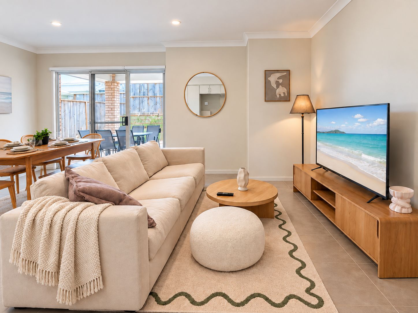 A living room with a sofa, a round coffee table, a TV, and a dining area with chairs and a table.