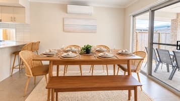 A dining area with a wooden table set for four, surrounded by wicker chairs, a bench, and a view through a glass door.