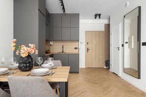 A modern kitchen with grey cabinets, a wooden dining table set with plates and glasses, and a vase with flowers. - Katowice | Zabrska 15 | Modern Apartment | Air conditioning (Katowice)