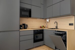 The L-shaped layout of a kitchenette includes built-in black appliances, maximizing both style and functionality.  - Katowice | Zabrska 15 | Modern Apartment | Air conditioning (Katowice)