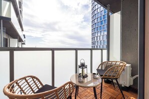 Ein Balkon mit zwei Korbstühlen, einem Glastisch, einer Kerze und einer Kaffeetasse.