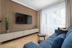 Ein modernes Wohnzimmer mit Flachbildfernseher an einer Wand aus Holzleisten, einem blauen Sofa und einem kleinen Beistelltisch mit einem Buch.