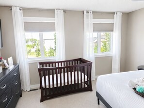 A bedroom with a crib, a bed, a dresser, and two windows with curtains. - Elegant and Spacious Getaway in St. Albert. 4 BR's, AC and Premium Amenities. (St. Albert)