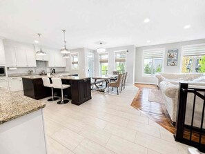 A modern kitchen with white cabinets, a central island, bar stools, and pendant lighting. - Elegant and Spacious Getaway in St. Albert. 4 BR's, AC and Premium Amenities. (St. Albert)