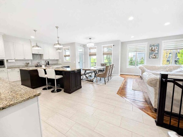 A modern kitchen with white cabinets, a central island, bar stools, and pendant lighting. - Elegant and Spacious Getaway in St. Albert. 4 BR's, AC and Premium Amenities. (St. Albert)