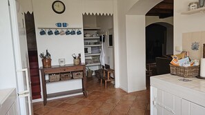 Una cocina con un banco de madera, estantes con utensilios de cocina y un piso de baldosas.