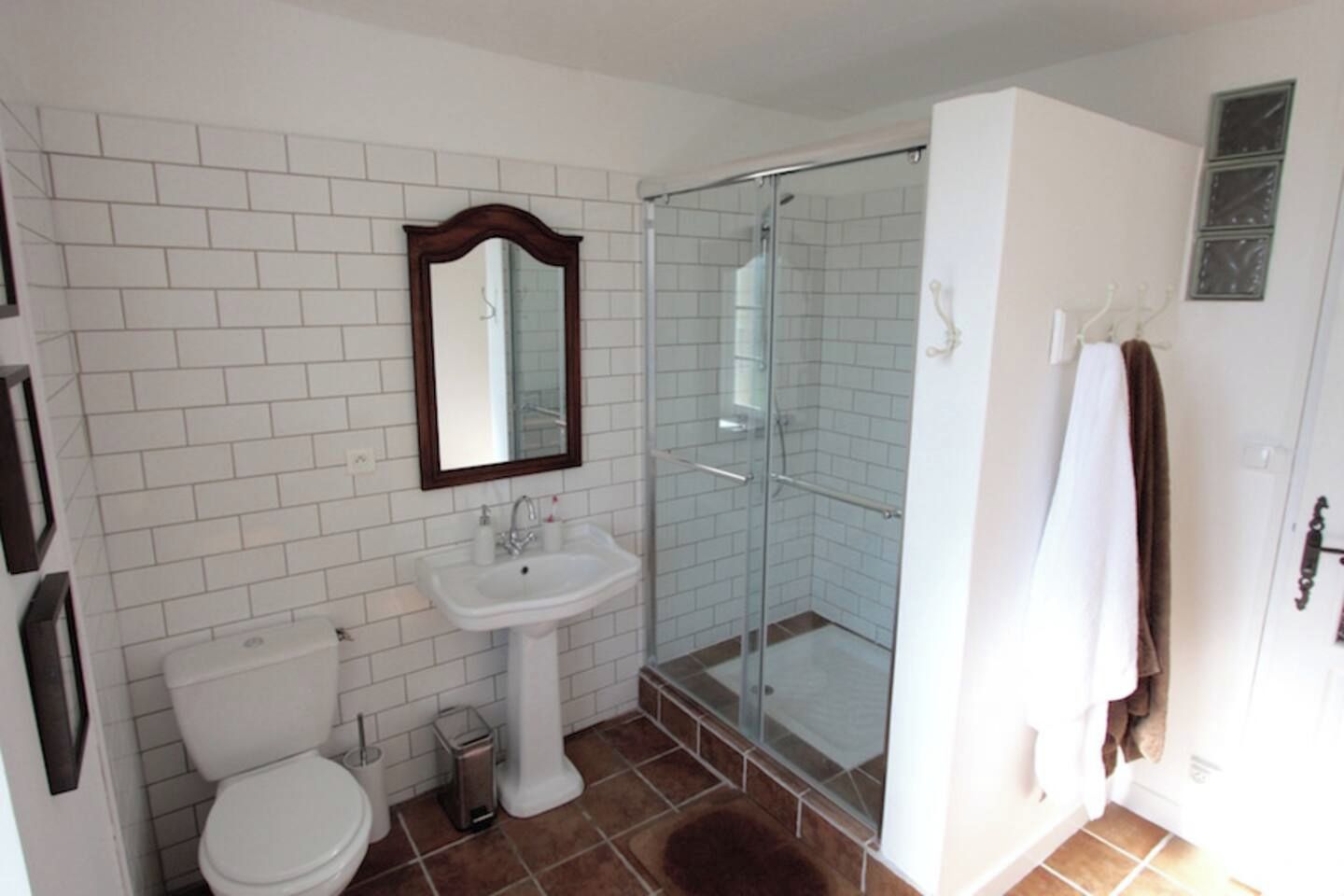 Ein Badezimmer mit Toilette, Waschbecken mit Standfuß, einer Duschkabine und einem Spiegel über dem Waschbecken.