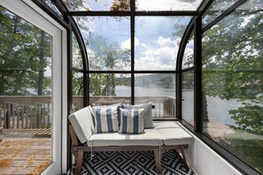 A covered seating area with a bench and cushions, overlooking a body of water and trees.