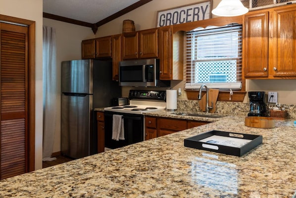 A kitchen with wooden cabinets, a stainless steel refrigerator, a microwave, a stove, and a granite countertop.