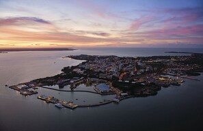 Luchtbeeld van een kuststad met een jachthaven, gebouwen en een zonsondergang.