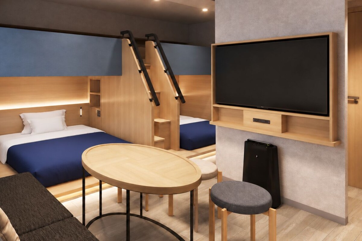 A modern hotel room with a bed, a desk, a chair, a TV, and a staircase.