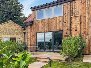A modern building with wooden paneling, large glass windows, and a stone structure to the left. - Coach House - UK52274 (Helmsley)