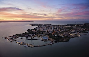 Ett flygbildsbild av en kuststad med en småbåtshamn, byggnader och en solnedgångshimmel.