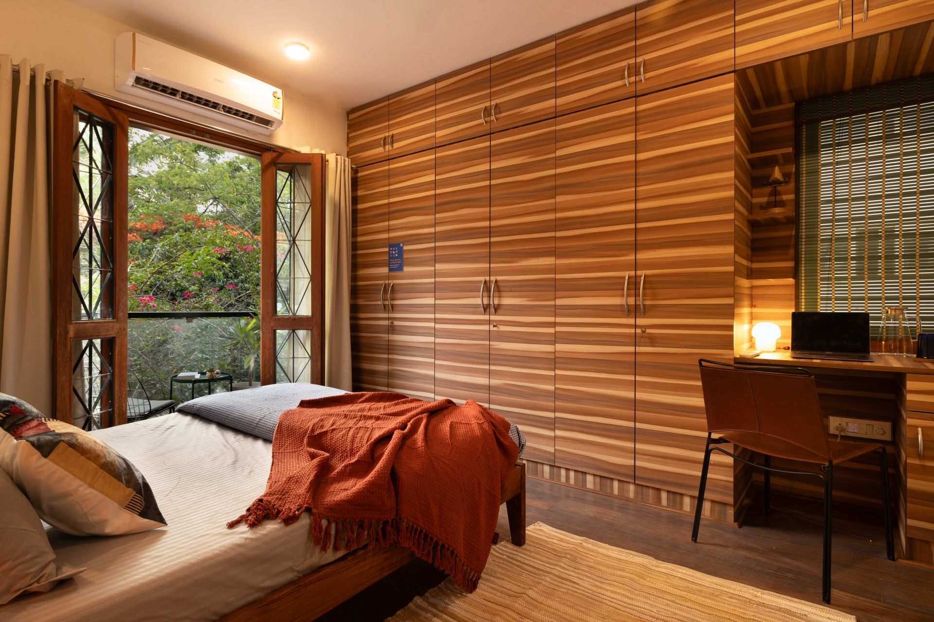 A bedroom with a bed, a desk, and a view of greenery outside.