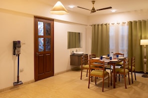 A hotel room with a dining area, a ceiling fan, a window with curtains, and a door with a stained glass design. - LiveAway Bengaluru (HSR) by PACK (Bengaluru)
