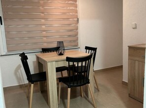 A dining area with a wooden table and black chairs, a window with blinds, and a wooden cabinet. - Apartments Adriana - Two Bedroom Apartment 10 (Gradac)
