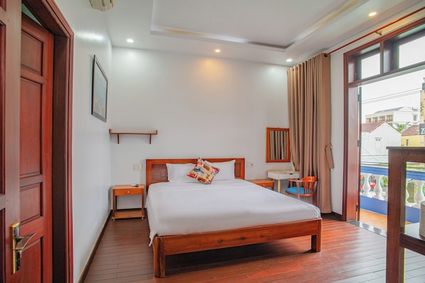A hotel room with a wooden bed, a nightstand, a desk, a chair, and a large window with curtains. - QUA CAM TIM HOMESTAY (HOI AN)