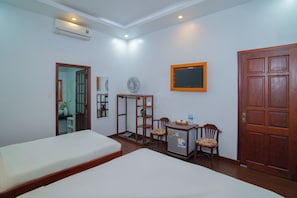 A hotel room with two beds, a desk with a chair, a small refrigerator, a wall-mounted TV, and a door. - QUA CAM TIM HOMESTAY (HOI AN)