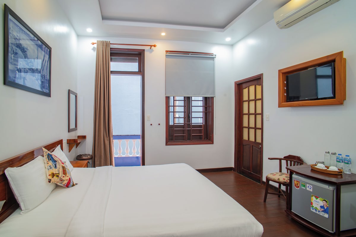 A hotel room with a bed, a desk with a computer, a television, and a window with curtains.