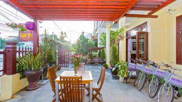 Un patio couvert avec une table et des chaises, des plantes en pot et des vélos.