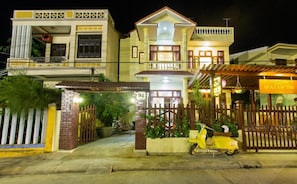 A two-story building with a gated entrance, a scooter parked in front, and a sign indicating a restaurant. - QUA CAM TIM HOMESTAY (HOI AN)