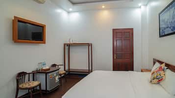 A hotel room with a bed, a desk with a chair, a wardrobe, a television, and a door.