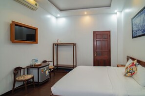 A hotel room with a bed, a desk with a chair, a wardrobe, a television, and a door. - QUA CAM TIM HOMESTAY (HOI AN)