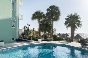 Ein Swimmingpool mit Liegestühlen und Palmen, mit Blick auf einen Strand.