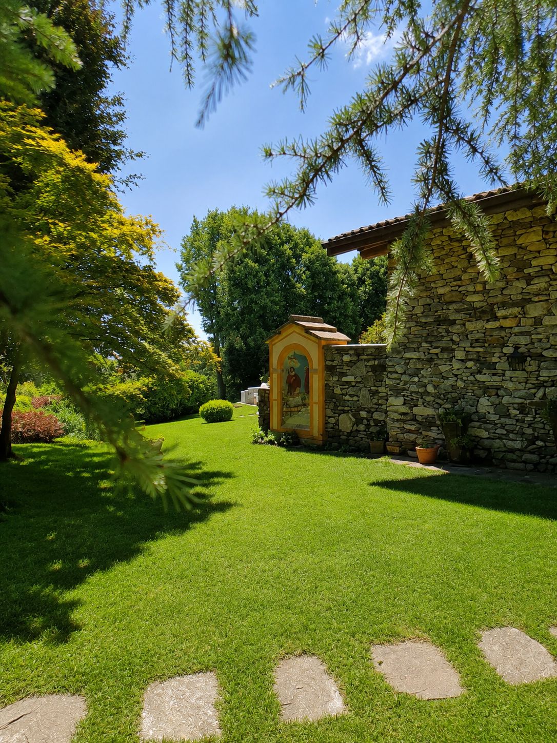 Un edificio in pietra con un piccolo ingresso ad arco, circondato da erba curata e alberi.