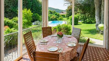 Veranda coperta con tavolo apparecchiato per mangiare, circondata da sedie, affacciata su piscina e giardino.