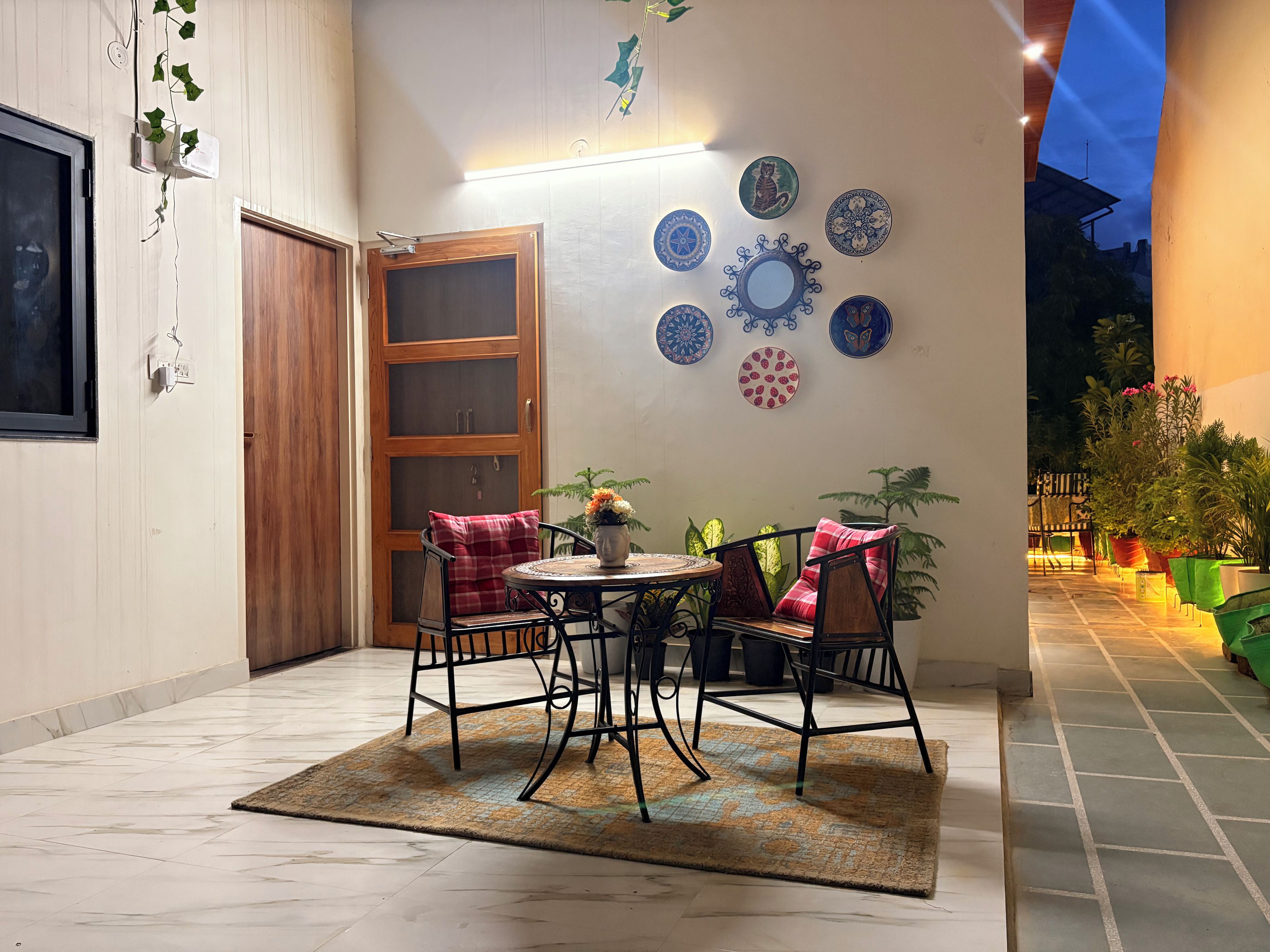A cozy patio area with a round table, two chairs, a wooden door, and decorative plates on the wall.