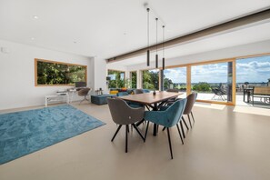 A modern dining area with a large table and chairs, a blue rug, and a view of the outdoors through large windows. - 25 Min to Munich Luxury 370 m² 4,000 sqft Villa Aircon + Heat Pump (Eching)