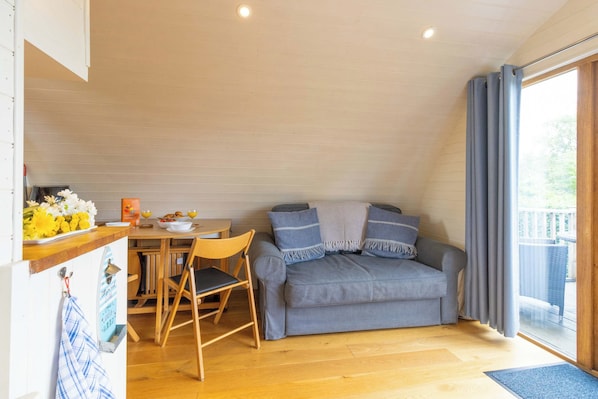 A cozy room with a dining area, a sofa, and a view of the outdoors. - Riverside Glamping Pod with Free WiFi & Parking (Garth)