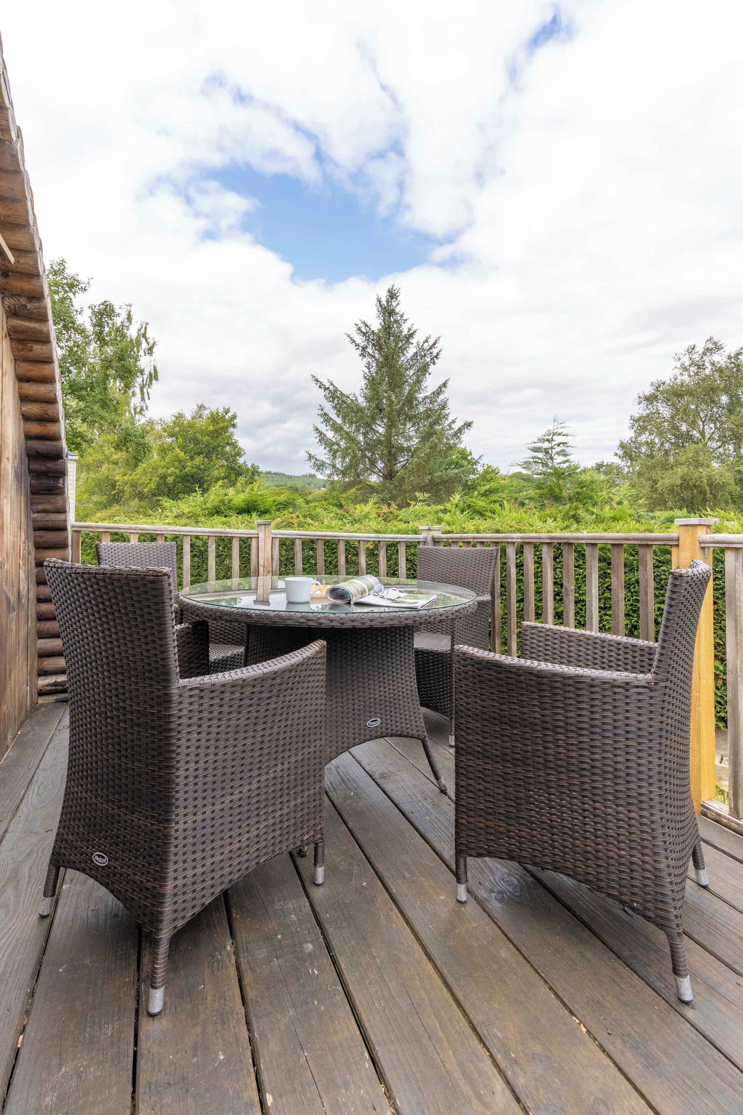 A wooden deck with wicker furniture and a glass table.
