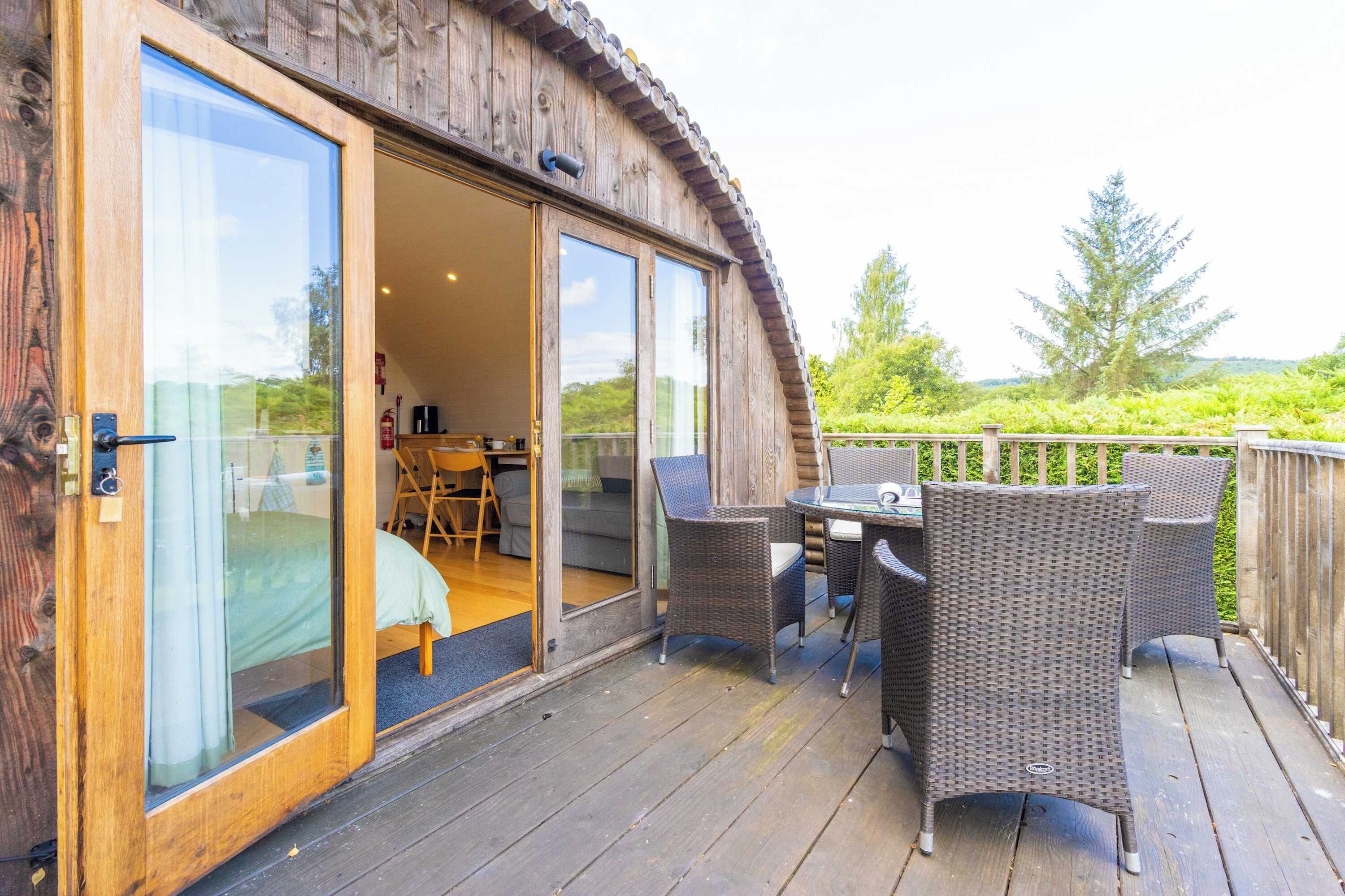 A wooden deck with wicker furniture and a glass door leading to an interior space with a sofa and a table.