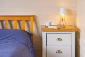 Ein Bett mit Holz Kopfteil, ein Nachttisch mit Lampe, eine Tasse und ein Buch.