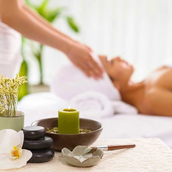 A massage therapy session with a person lying on a massage table, a candle, stones, and a flower arrangement.