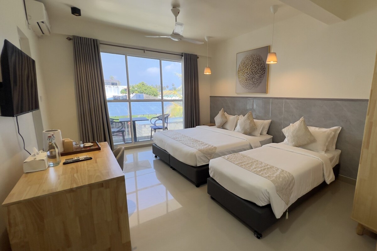 A hotel room with two beds, a desk with a computer, a TV, and a view of the outdoors.