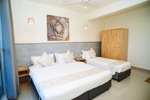 A hotel room with two beds, a wooden wardrobe, a ceiling fan, and a wall-mounted artwork.
