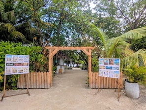 A wooden archway with a signboard on each side, leading to a pathway surrounded by lush greenery.