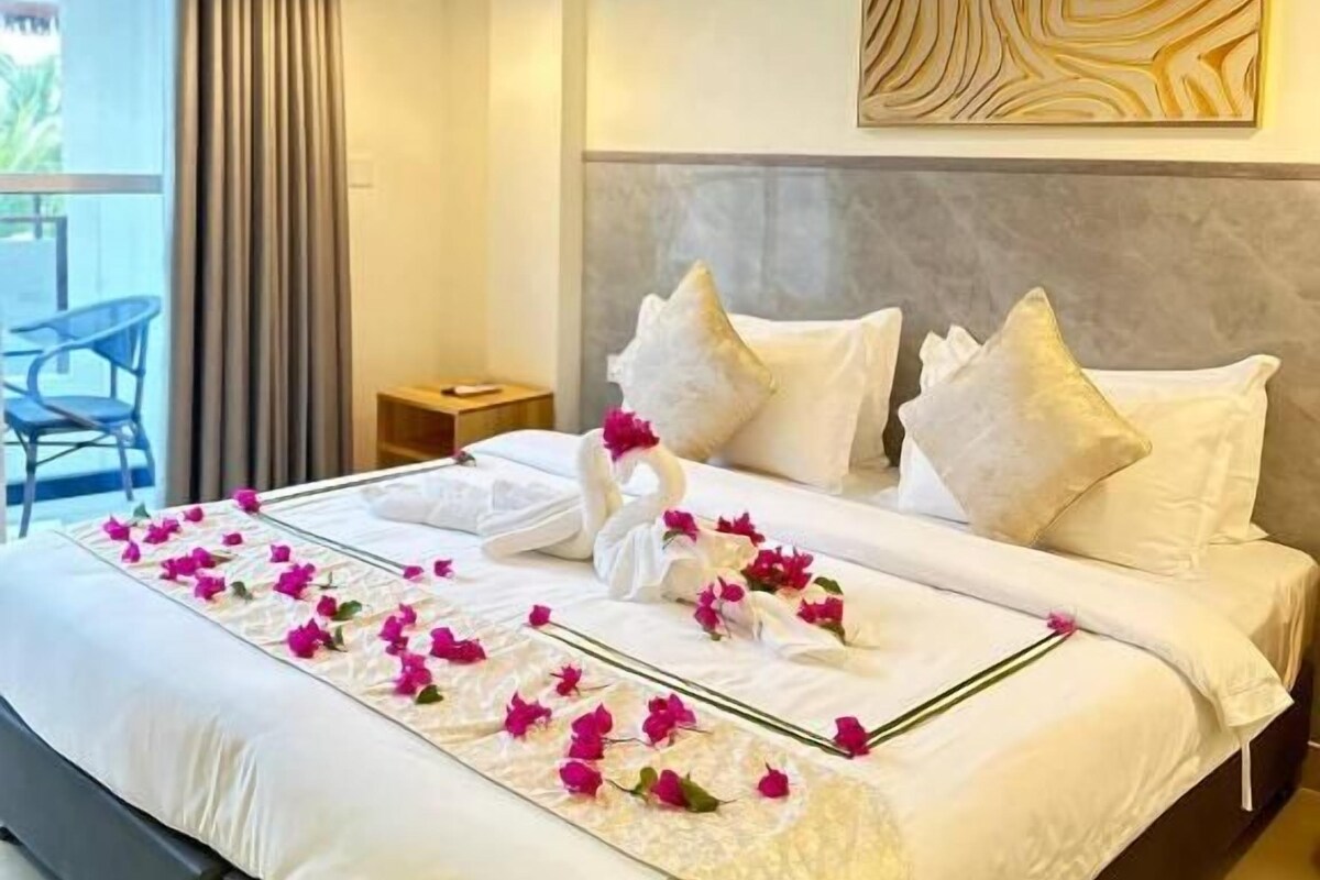 A hotel room with a bed, a nightstand, a wall-mounted artwork, and a view through a window.