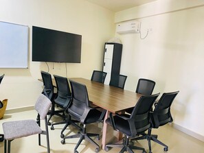A conference room with a long table, black chairs, a whiteboard, and a white air conditioning unit. - YUVi blue maldives (Himmafushi)